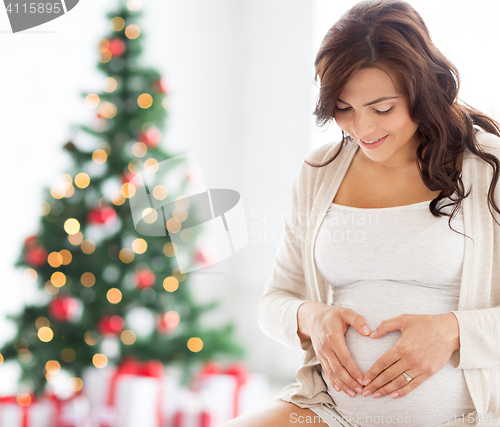 Image of happy pregnant woman making heart gesture at home