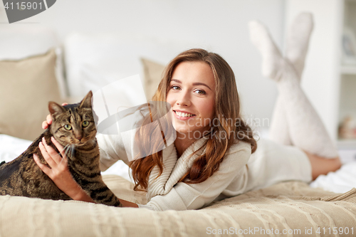 Image of happy young woman with cat lying in bed at home