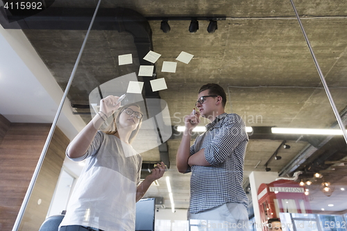 Image of young couple at modern office interior writing notes on stickers