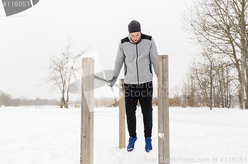 Image of young man exercising on parallel bars in winter