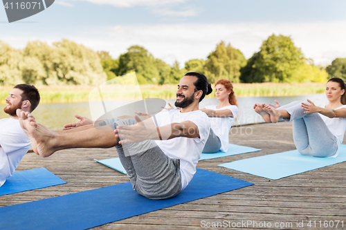 Image of people making yoga in half-boat pose outdoors