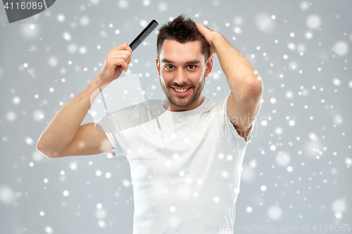 Image of happy man brushing hair with comb over snow