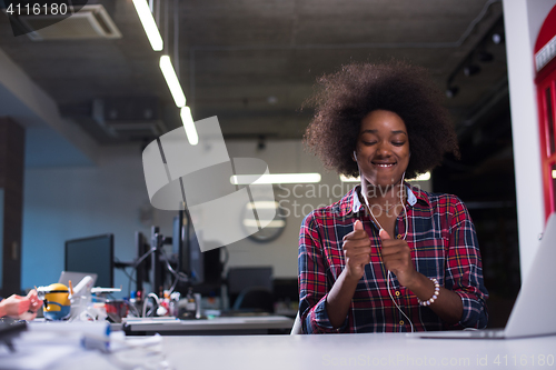 Image of black woman in modern office speeking on phone over earphones