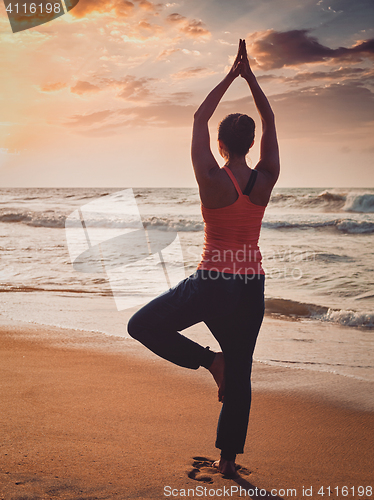 Image of Young sporty fit woman doing yoga tree asana on beach