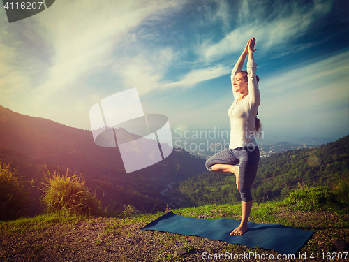 Image of Woman in  yoga asana Vrikshasana tree pose in mountains outdoors