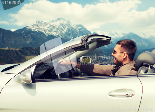 Image of happy man driving cabriolet car over mountains