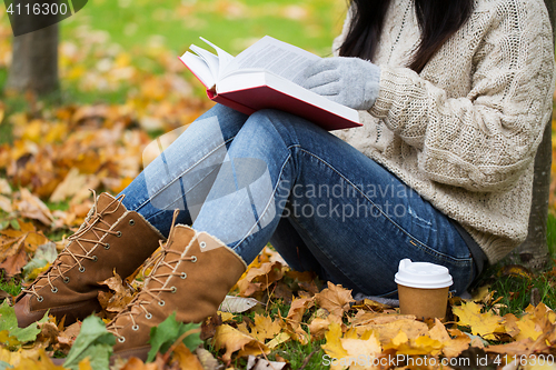 Image of woman with book drinking coffee in autumn park