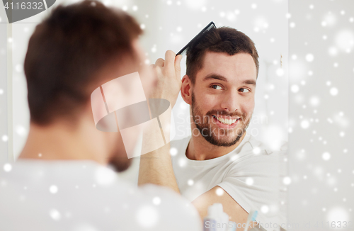 Image of happy man brushing hair with comb at bathroom