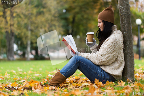 Image of woman with book drinking coffee in autumn park