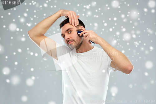 Image of smiling man shaving beard with trimmer over snow