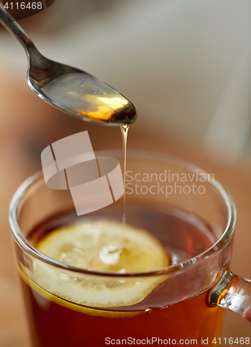 Image of close up of woman adding honey to tea with lemon