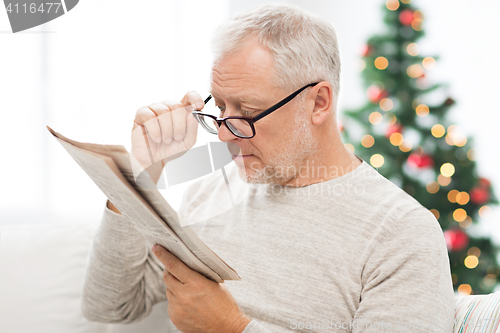 Image of senior man in glasses reading newspaper at home