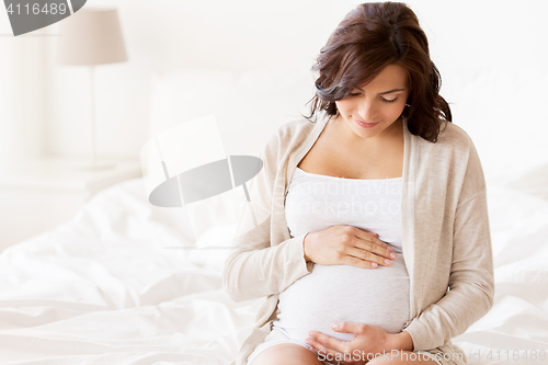 Image of happy pregnant woman sitting on bed at home