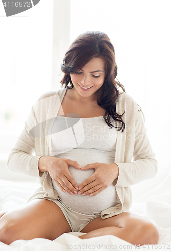 Image of happy pregnant woman making heart gesture at home