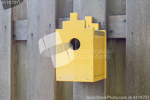 Image of Yellow birdhouse on a wooden fence