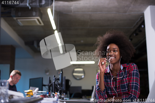 Image of black woman in modern office speeking on phone over earphones