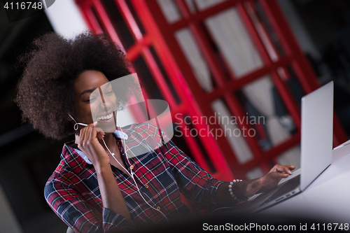 Image of black woman in modern office speeking on phone over earphones