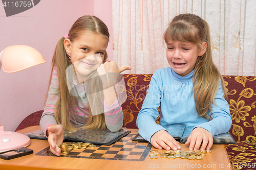 Image of Two girls at the table collected montki one cries, the other laughs at it