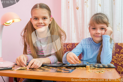 Image of Two children are considered a collection of coins in albums