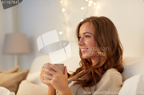 Image of happy woman with cup of coffee in bed at home