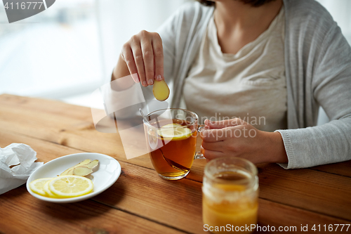 Image of close up of woman adding ginger to tea with lemon