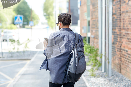 Image of man with backpack and smartphone walking in city