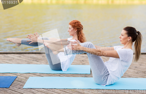 Image of women making yoga in half-boat pose outdoors