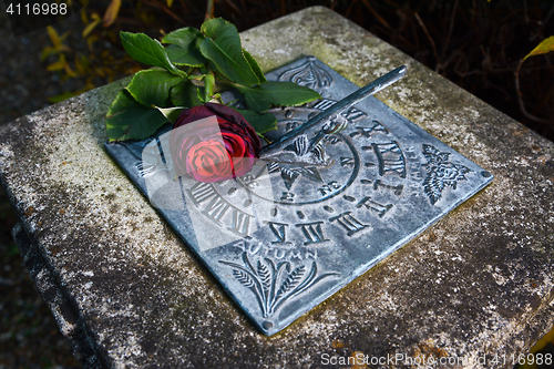 Image of Red rose lying on a weathered sundial