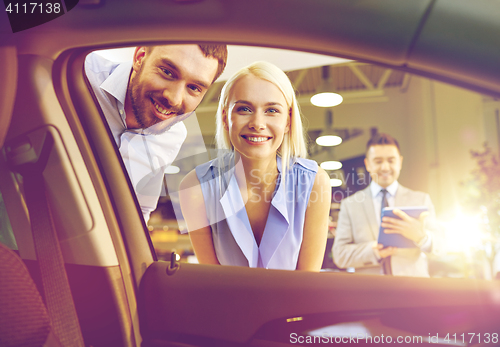 Image of happy couple with car dealer in auto show or salon