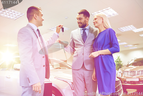 Image of happy couple with car dealer in auto show or salon