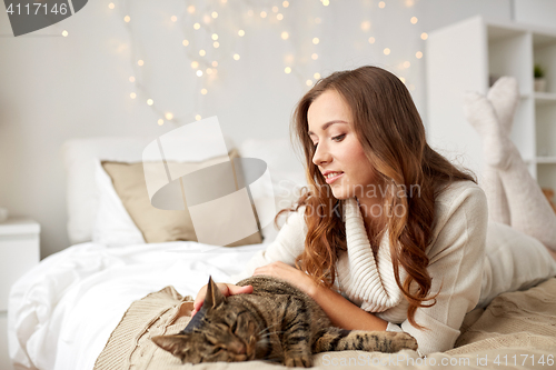 Image of happy young woman with cat lying in bed at home