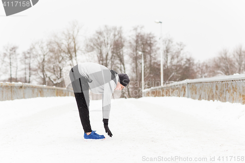 Image of man exercising and stretching leg on winter bridge