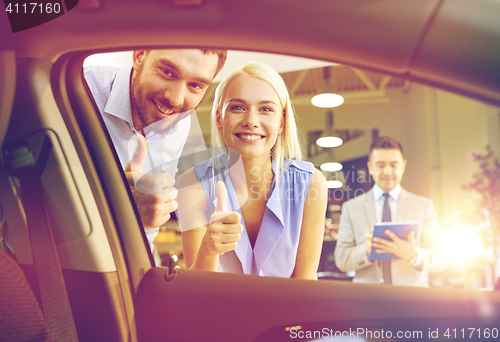 Image of happy couple with car dealer in auto show or salon