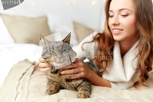 Image of happy young woman with cat lying in bed at home