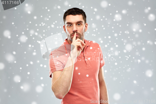 Image of young man making hush sign over snow background