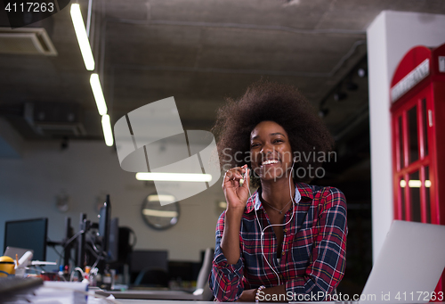 Image of black woman in modern office speeking on phone over earphones