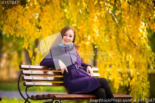 Image of Young girl sitting on the bench warm autumn day