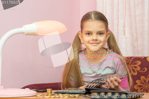 Image of The child leafing through an album for collectors of coins and looked into the frame