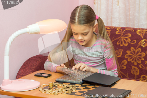 Image of Girl at the table leafing through the album with coins