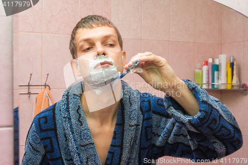 Image of Young guy shaves neck in front of the mirror