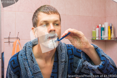 Image of Young man shaving in front of mirro