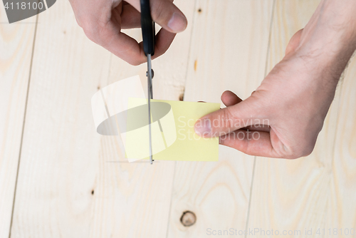 Image of A man is cutting a sheet of yellow paper using metallic scissors