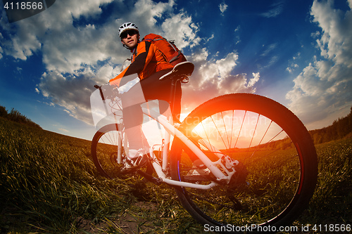 Image of biker in orange jersey riding on green summer field