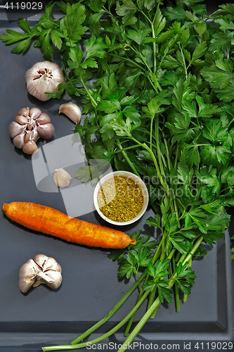 Image of Parsley leaves and vegetables on a dark tray.