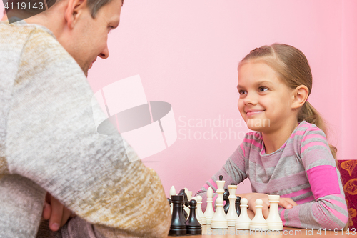 Image of Dad and daughter happily look at each other, playing chess