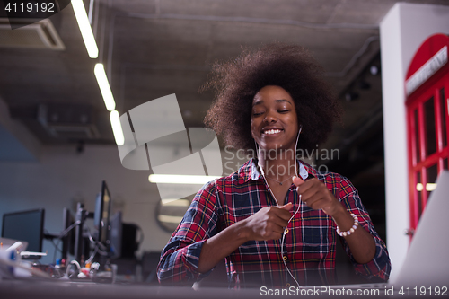 Image of black woman in modern office speeking on phone over earphones
