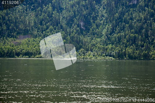 Image of boat goes along the shore of a mountain lake