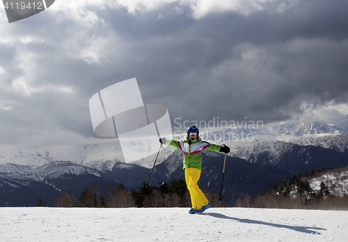 Image of Happy young skier with ski poles in sun mountains and cloudy gra