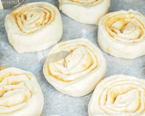 Image of Closeup of raw cinnamon roll and cinnamon buns on baking paper