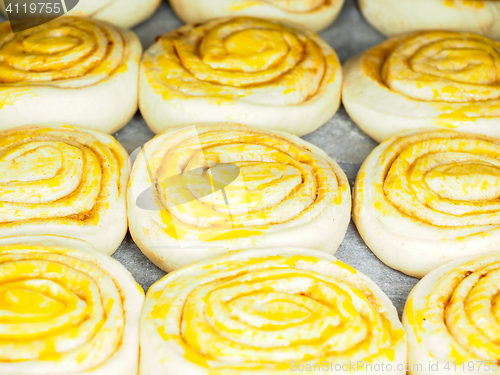 Image of Closeup of raw cinnamon buns after proofing with egg yolk, on ba